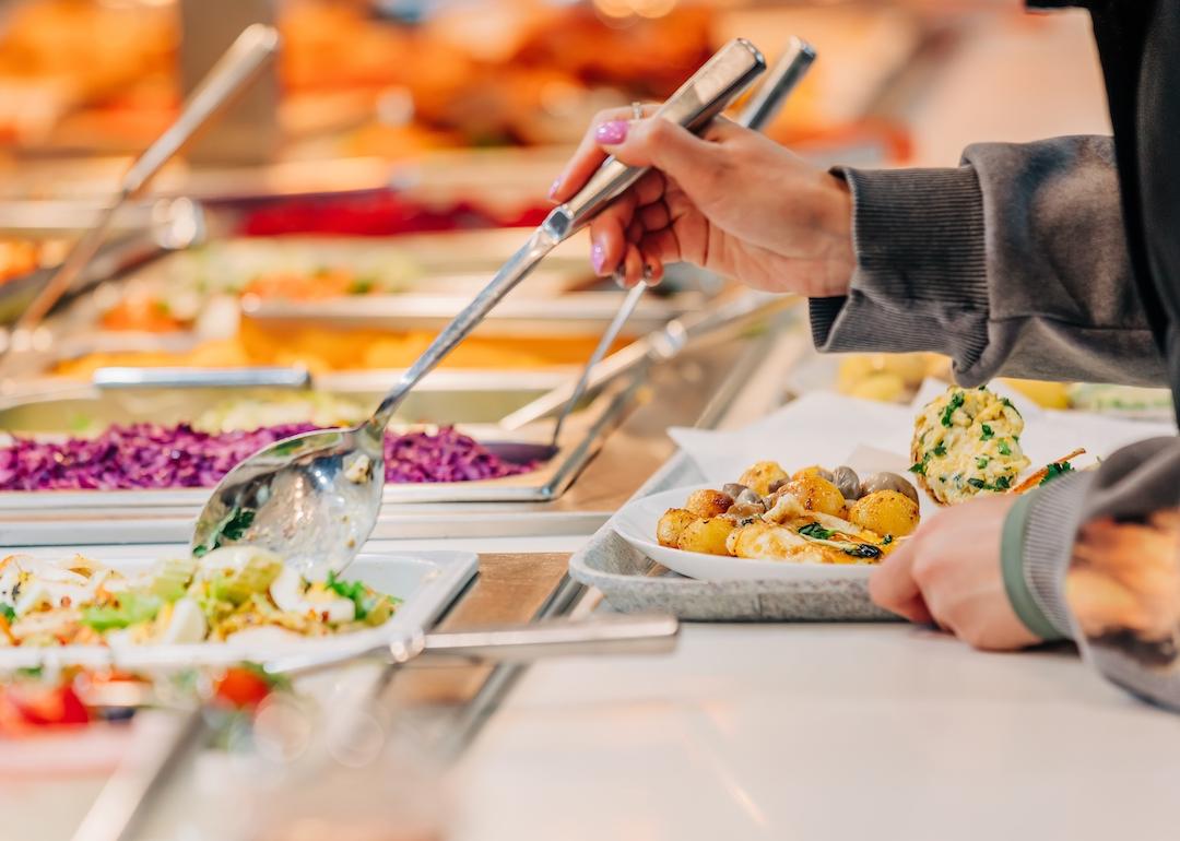 Person puts food on their plate at a buffet.