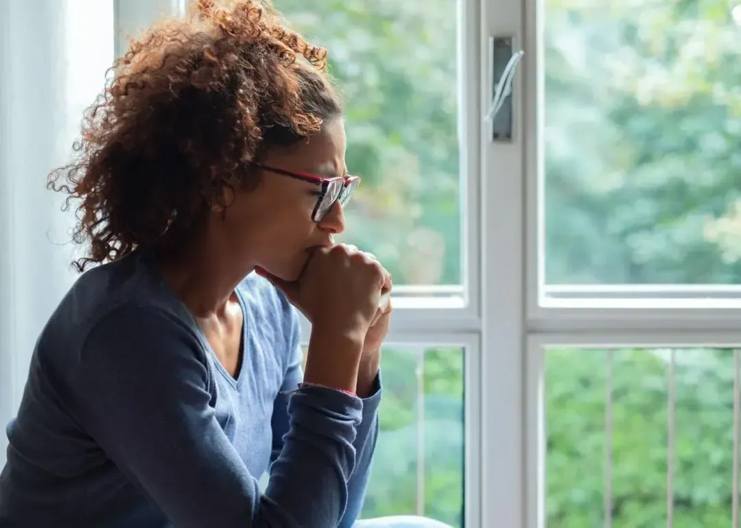 Person sitting by their window, looking sad and depressed.