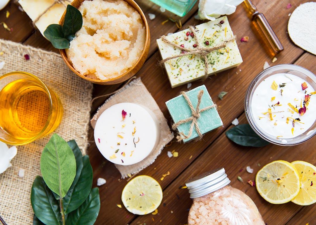 Top down view of lotions, soaps, and beauty products with flowers and plants incorporated on a wood table.