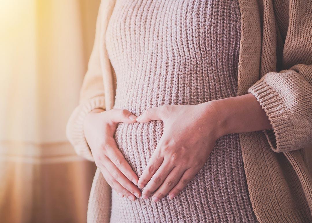 Photo of woman wearing a sweater dress holding hands over belly in a heart shape. 