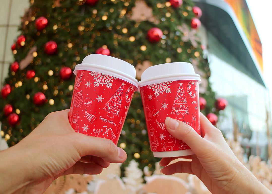 Holiday coffee cups are cheered in front of a Christmas tree.