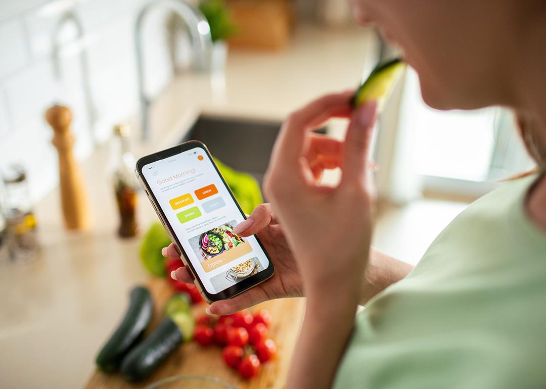 A woman is looking up meal plans on her phone while preparing food.