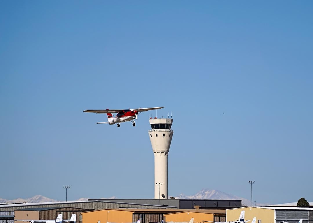 A single engine plane soaring near an airport control tower.