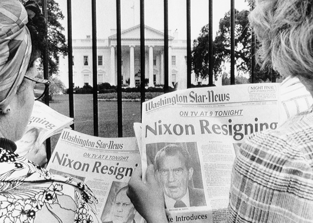 Newspaper headlines being read by tourists in front of the White House that says "Nixon resigns" circa 1974