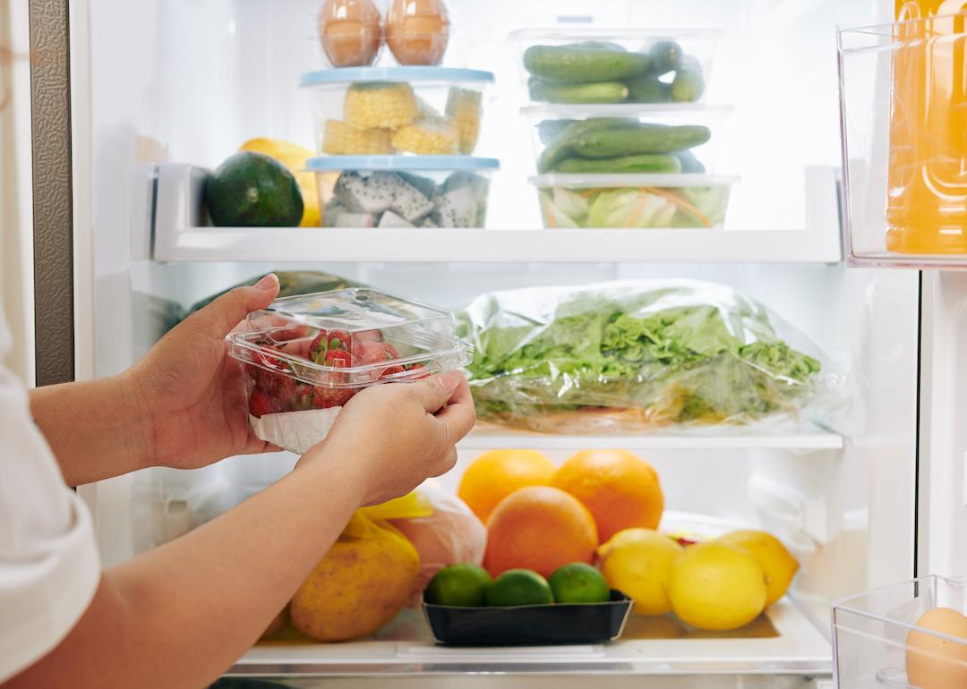 Person putting groceries away in fridge full of produce.