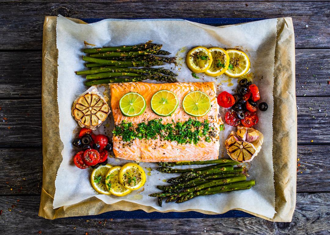 Roasted salmon steak with asparagus, lemon, rosemary, tomatoes, onion, and garlic on a sheet pan.