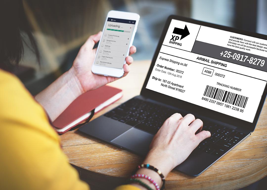 A woman using a laptop and phone to check a parcel's tracking number and progress.