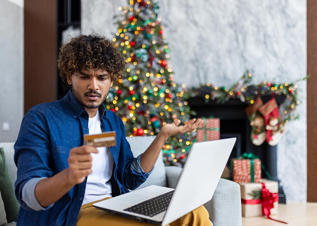 A guy looking confused at his credit card while online shopping for the holidays.