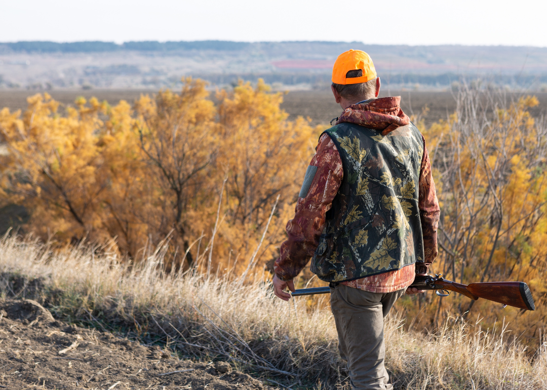 Hunter walking carrying a rifle on a sunny fall day