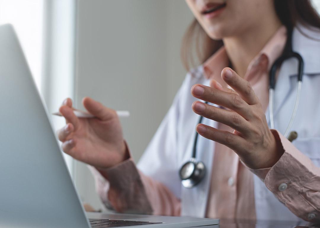 Generic medical professional (without face visible) gesturing in front of laptop computer.