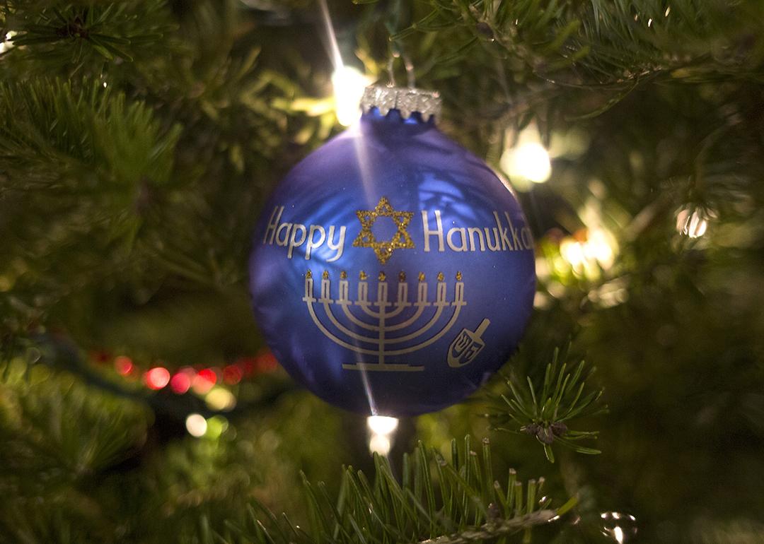 A blue "Happy Hanukkah" ornament hangs on a Christmas tree.