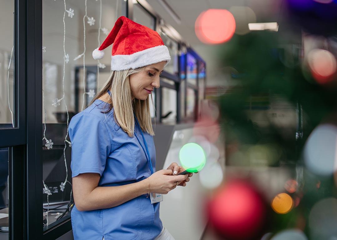 Medical professional in blue scrubs and a Santa hat texting in a holiday setting on break.