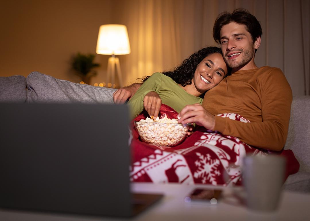 A couple eating popcorn enjoying a movie from a laptop during the holidays.