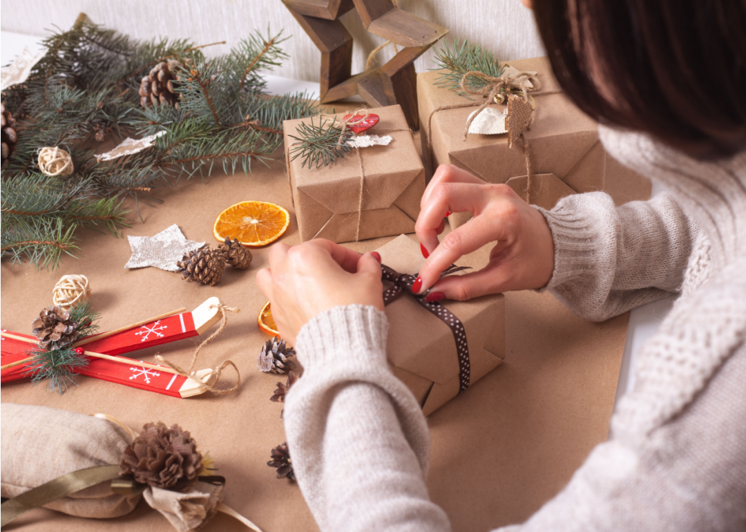 Woman wraps a Christmas present using brown craft paper with a fabric ribbon.