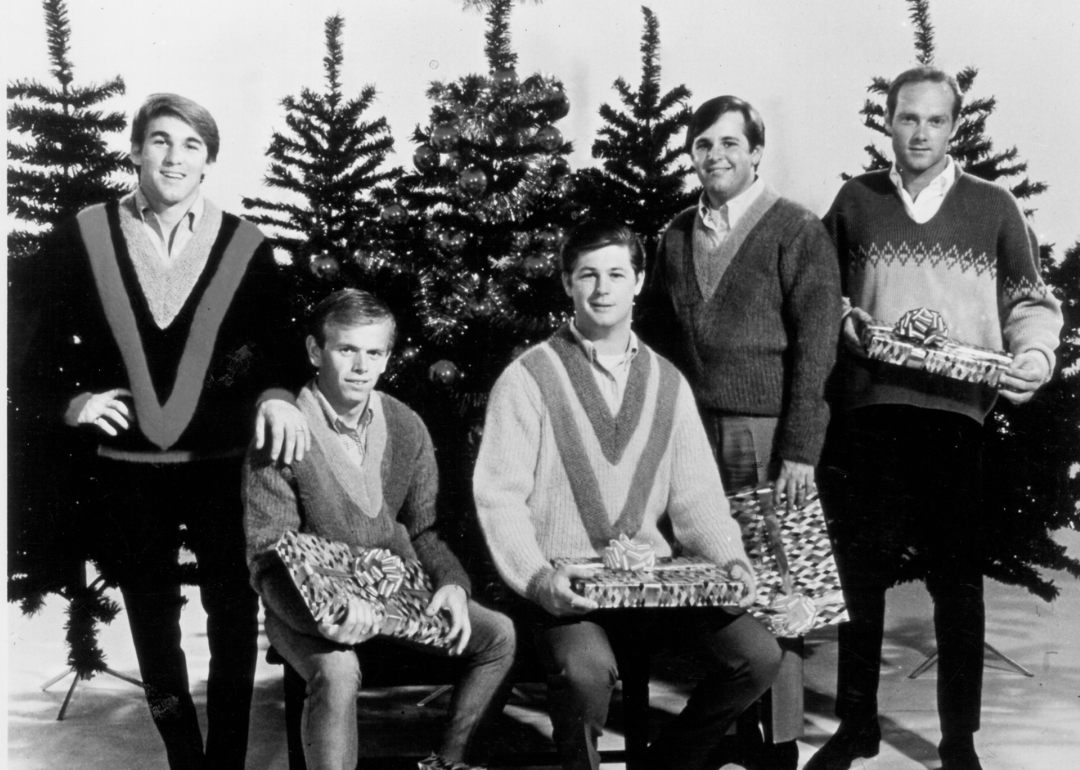 Rock and roll band "The Beach Boys" pose for a portrait in front of some Christmas trees holding presents in circa 1964.