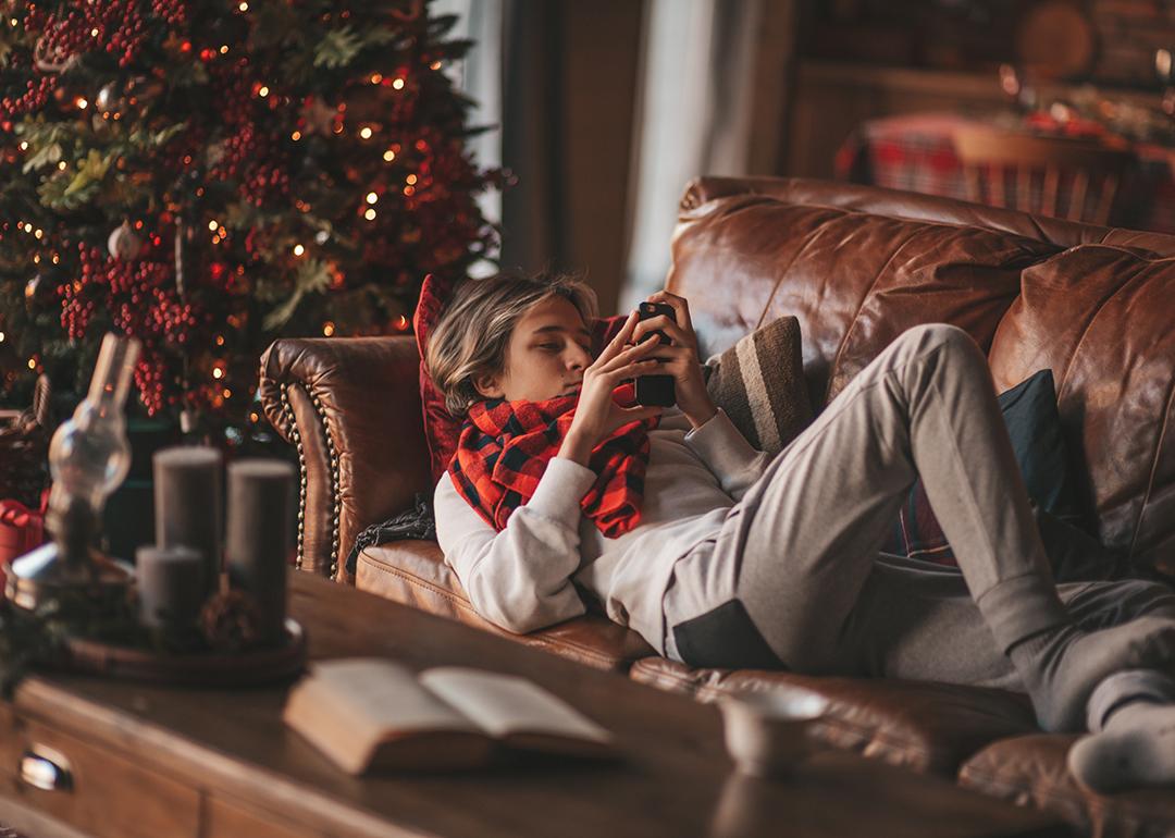 Young man lying on a couch and browsing his phone during Christmas eve.