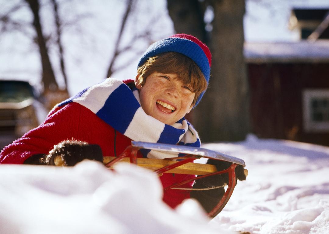 Smiling child sledding in the winter in the 1960s or '70s.