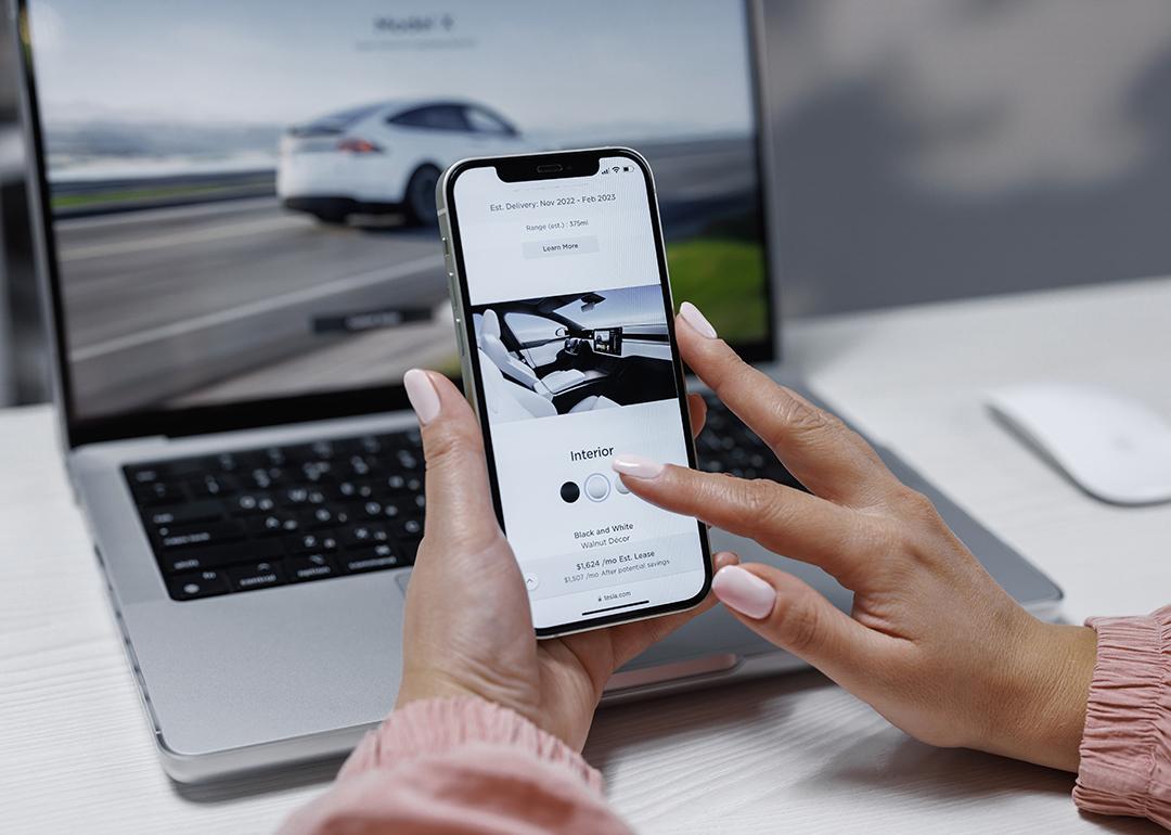 A woman is researching an EV using a laptop and phone.