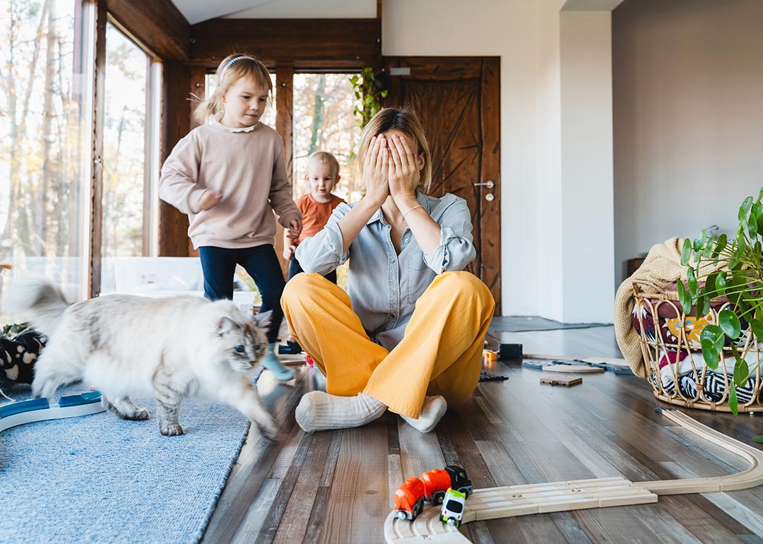 Stressed out mother sitting on the floor while kids are playing around.