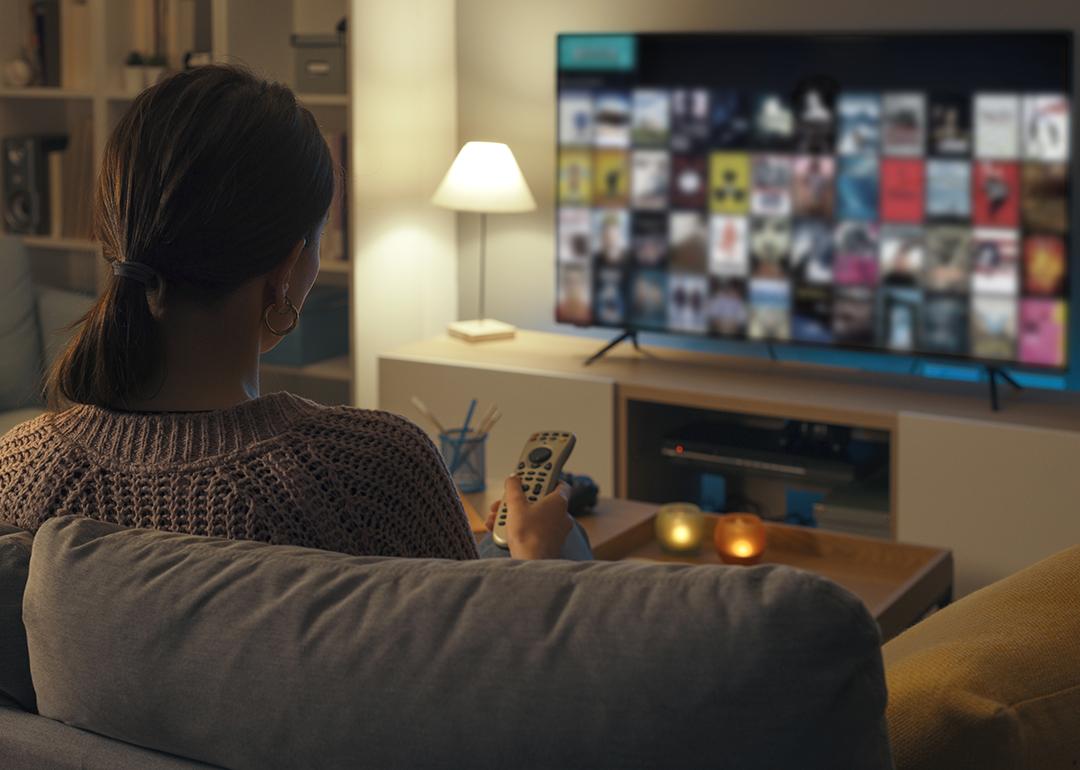 A woman relaxing at home is browsing through her smart TV looking for something to watch.