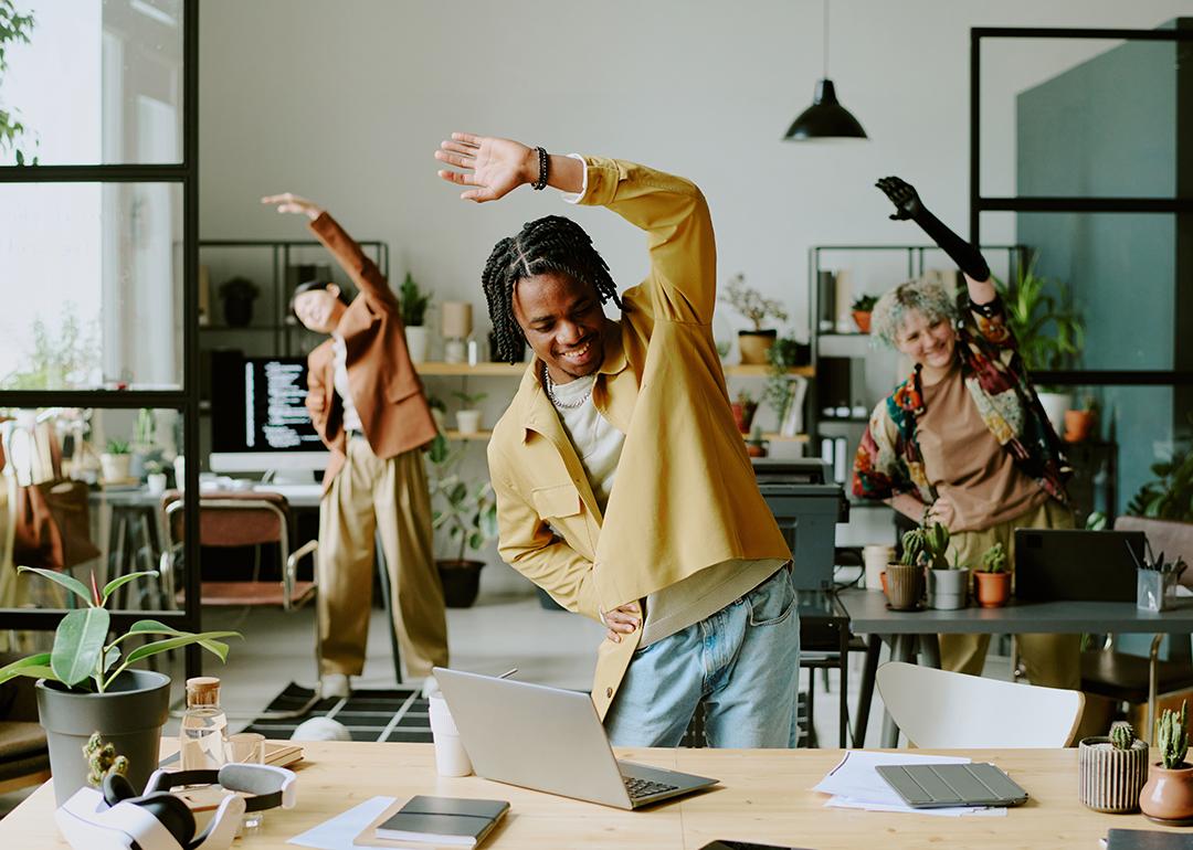 A group of happy ethnically diverse Gen Z coworkers doing morning exercise in a modern office. 