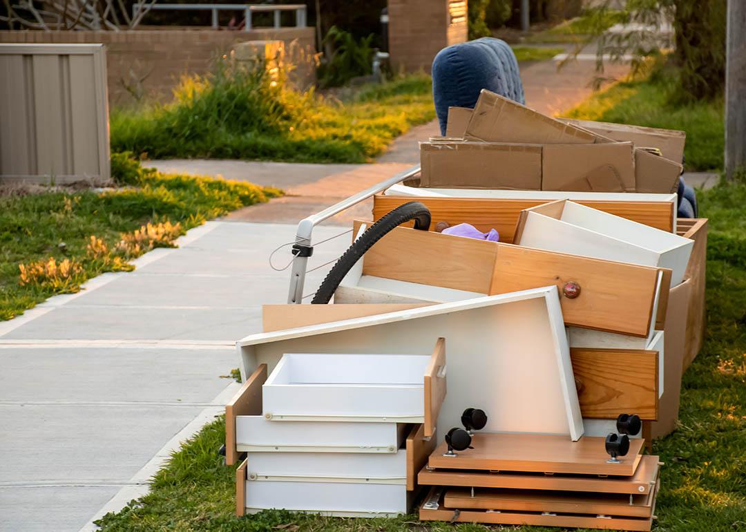 Discarded drawers, plywood furniture next to the sidewalk in morning light.