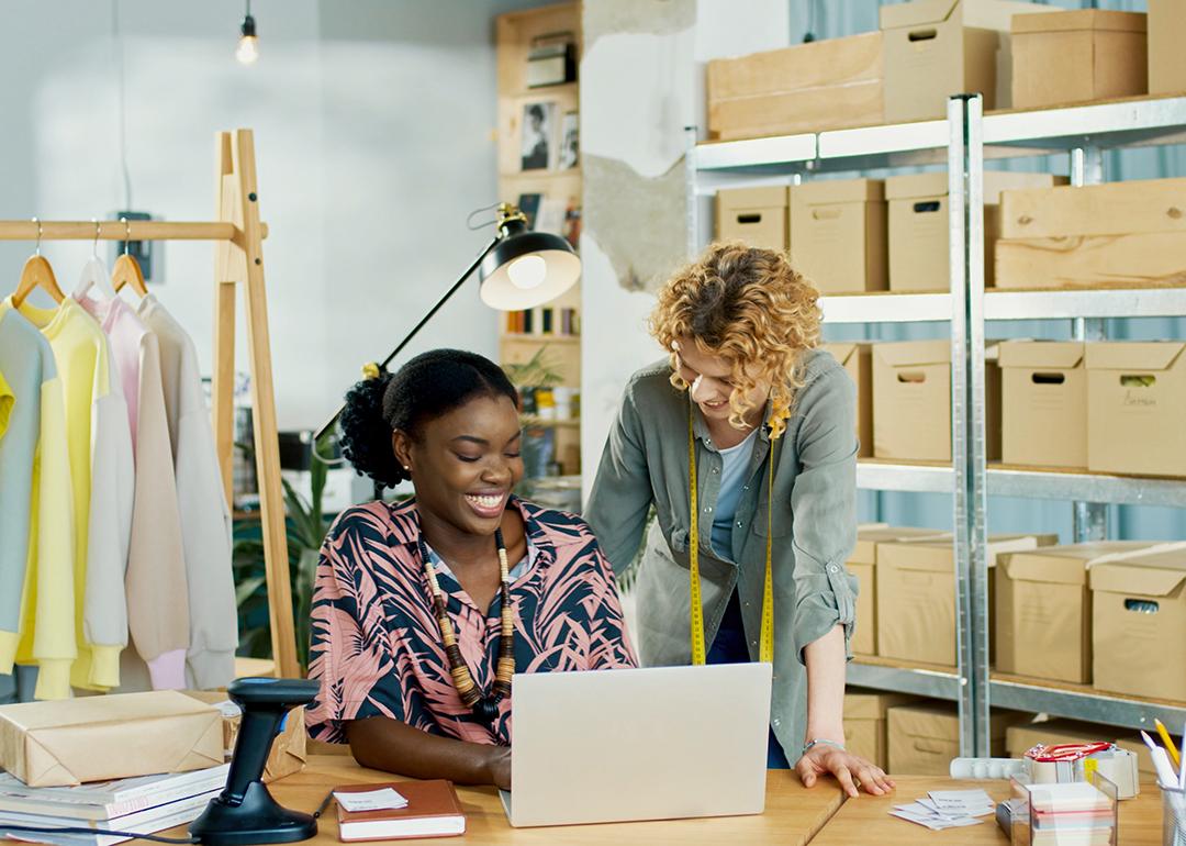 Two young women entrepreneurs who own a small clothing business happily looking at their laptop.