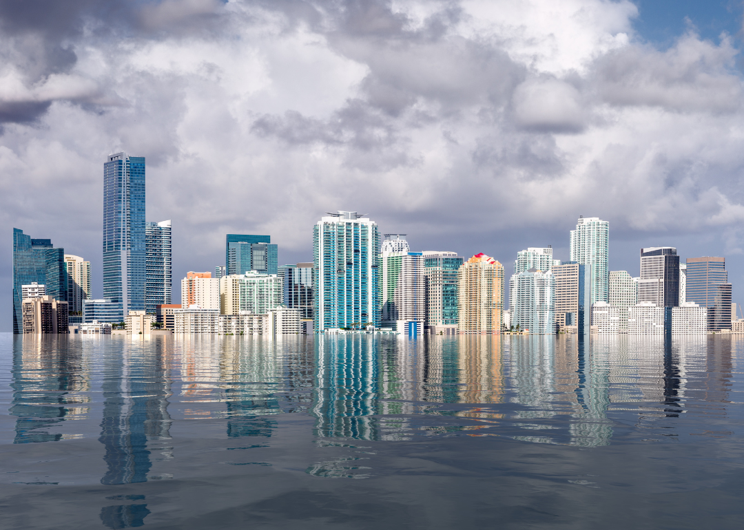 City skyline dots cloudy sky over flooded sea.