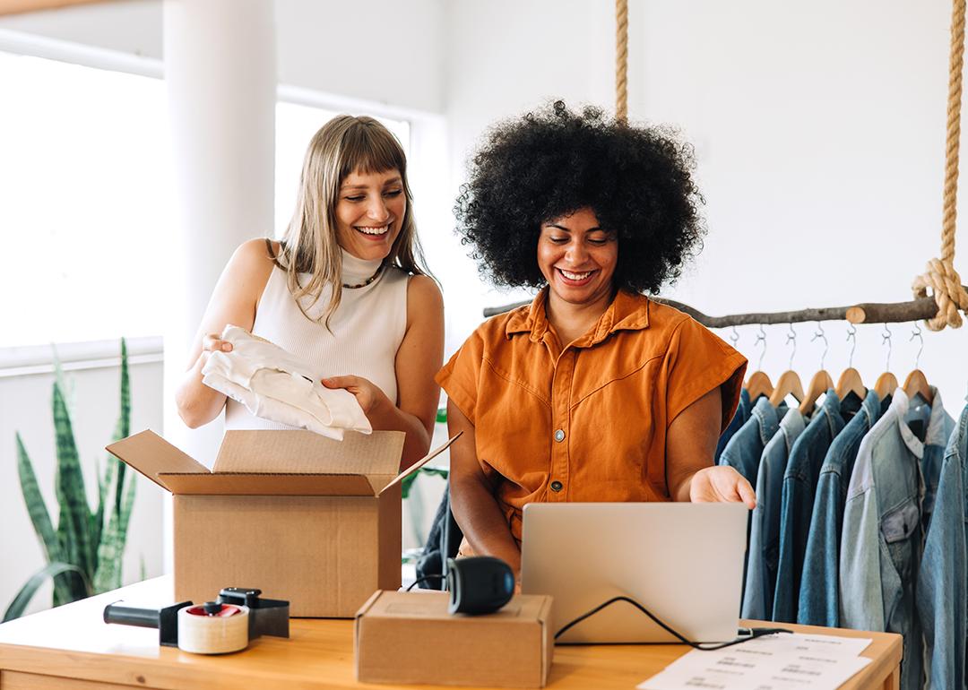 Two women who are owners of a clothing small business happily looking at orders from a laptop.