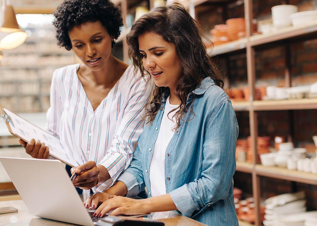 Two small business owners going through expenses, ceramics and products visible on shelves behind them.