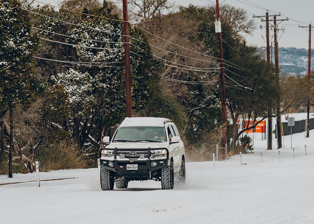 A white 4x4 truck braving thick snow on a Texas road after a blizzard.