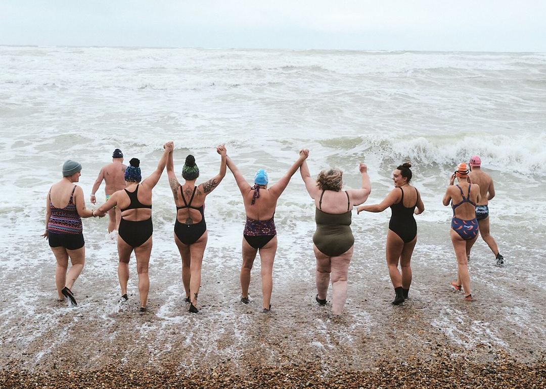 A group of nine adults happily going for a swim at the beach.