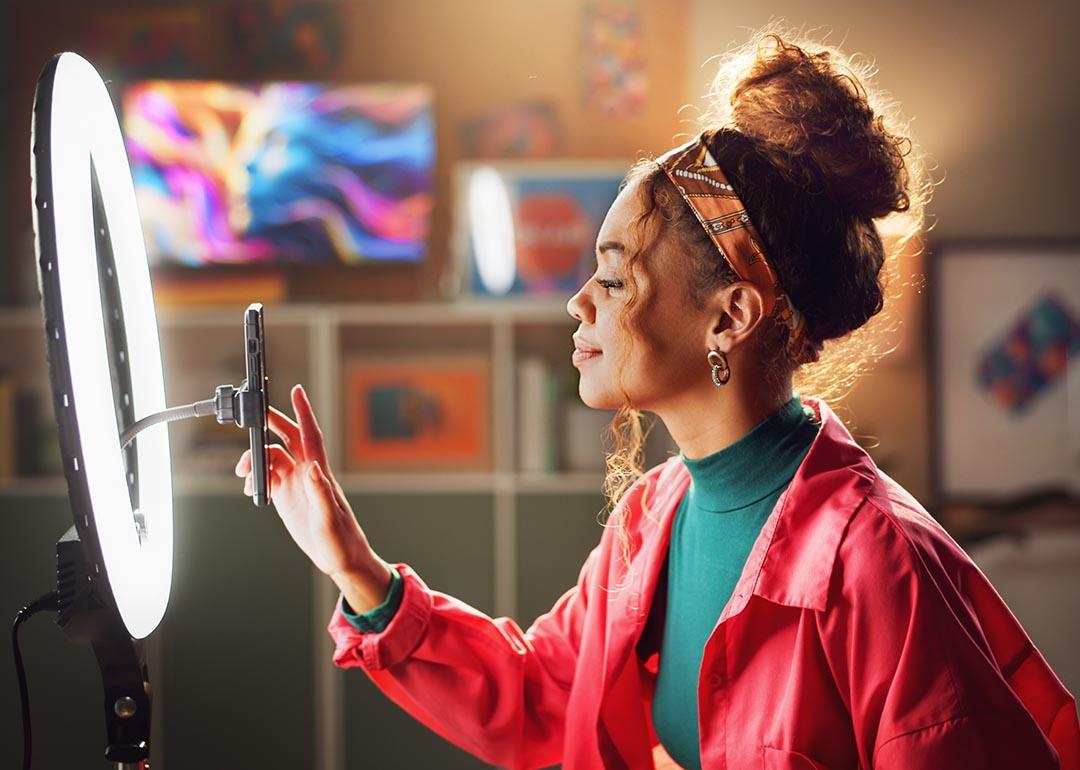 Woman using phone with mounted in a ring light to create content in a home studio setting.