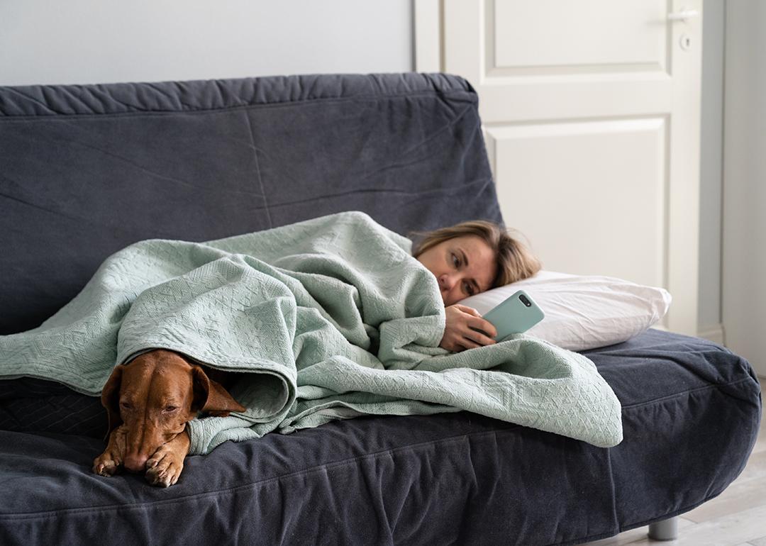 A lethargic woman lying on bed with her dog just looking at her phone.