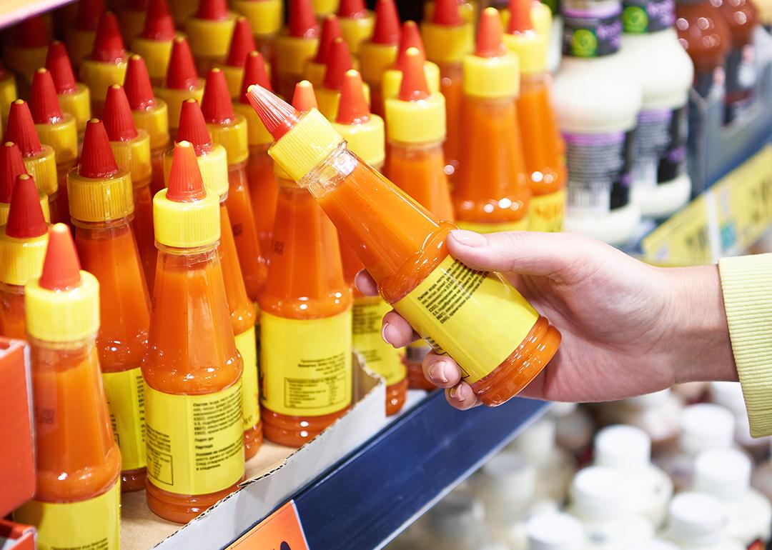 A customer choosing a bottle of hot sauce from its supermarket aisle.