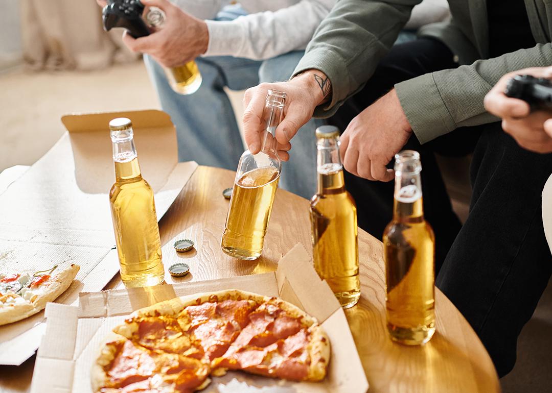 A group of three male friends consuming beer and eating pizza while playing video games.