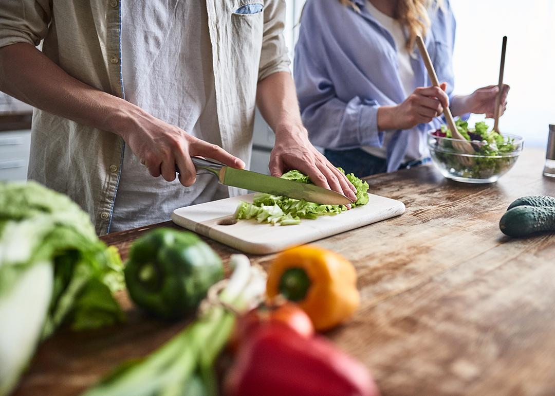 A couple preparing leafy green salad meals in the kitchen.