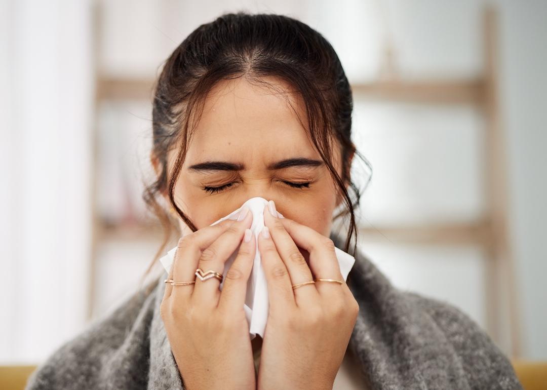 Sick person with COVID sneezing into tissue.