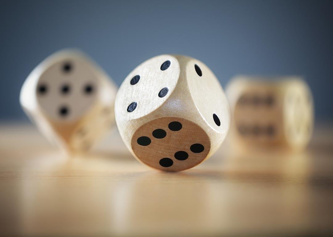 Close up of three wooden dice on a desktop, one in sharp focus, with a gray background.