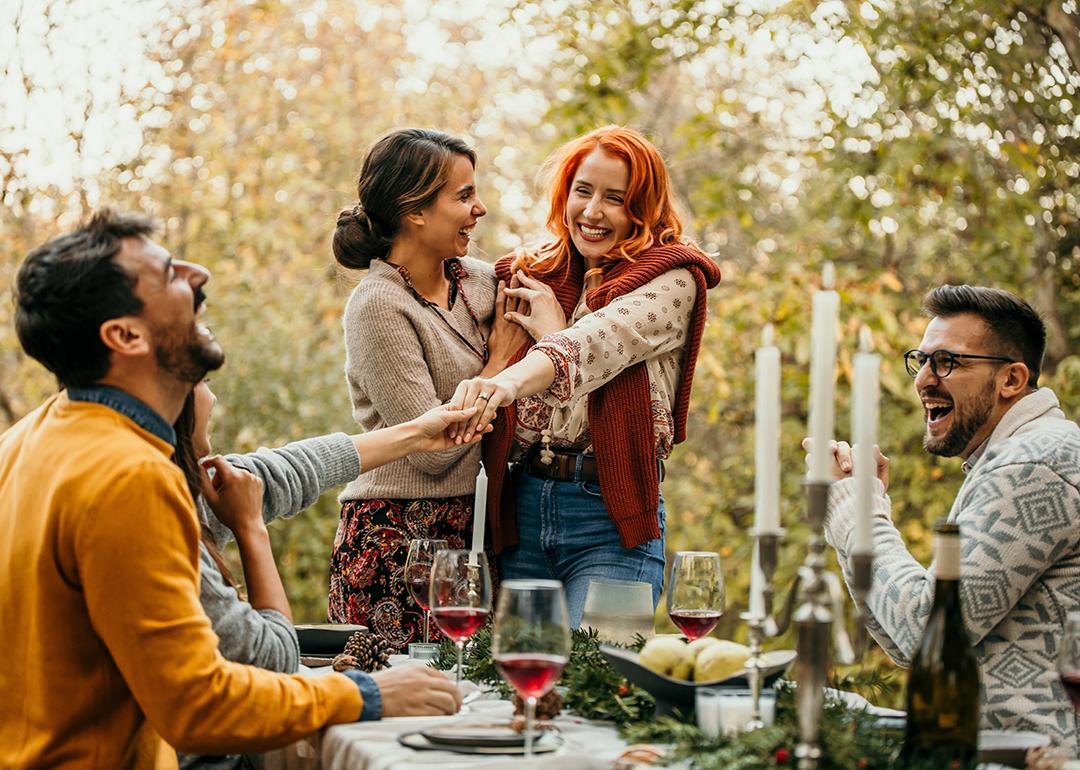 A lesbian couple showing off an engagement ring and celebrating a happy engagement with their friends.