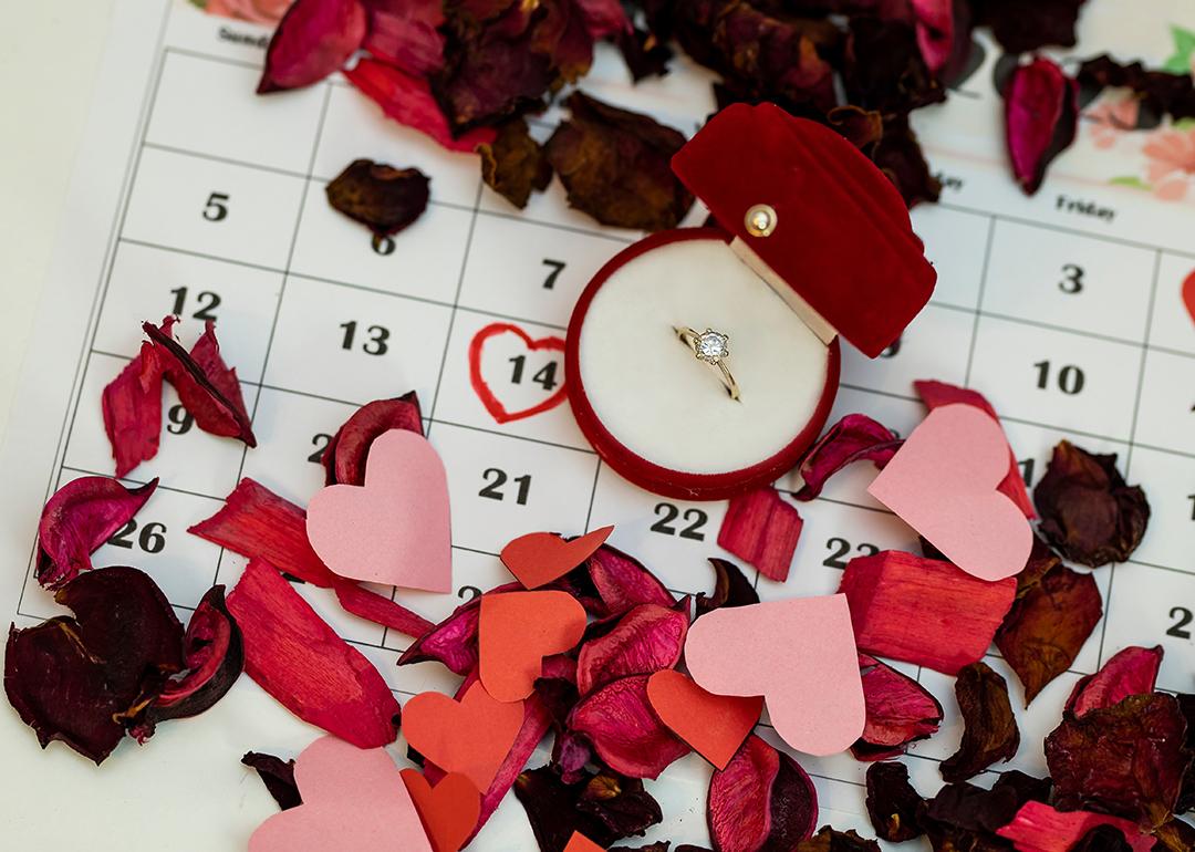 An engagement ring surrounded with rose petals on top of a calendar with February 14th circled.