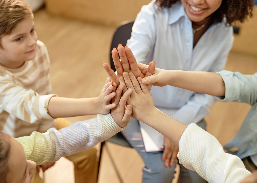 A group of children and a psychologist doing a high-five for great teamwork.