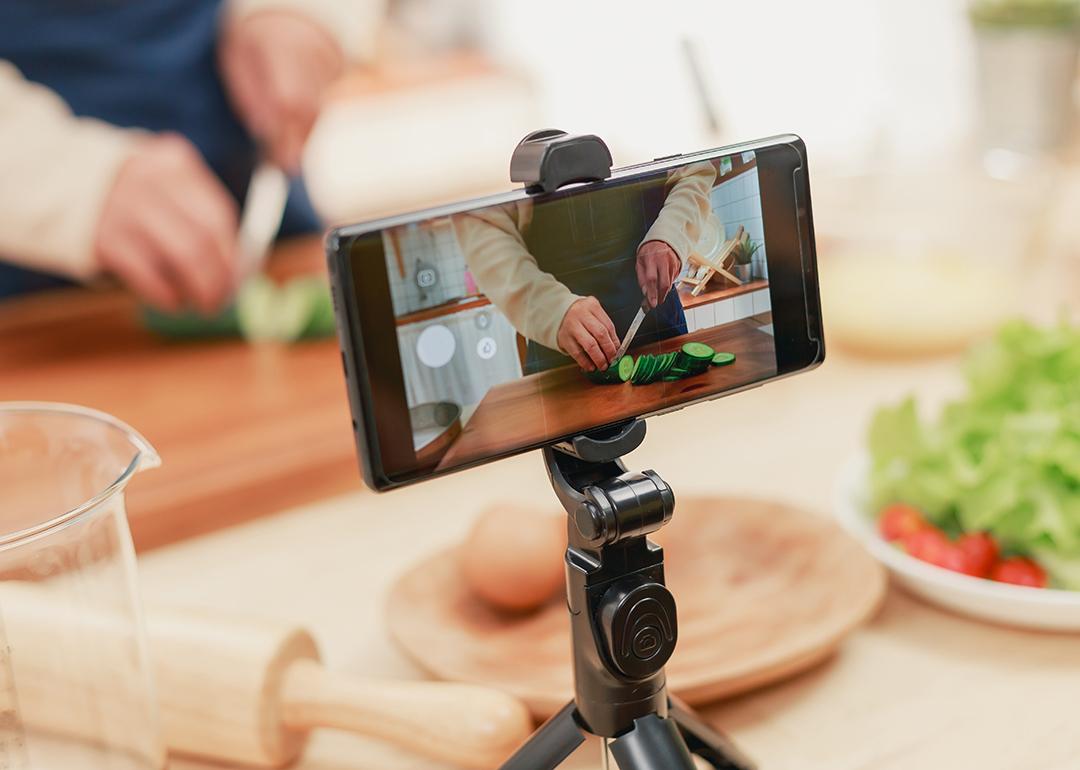 A male food influencer vlogging his cooking session at home using a phone on a tripod.