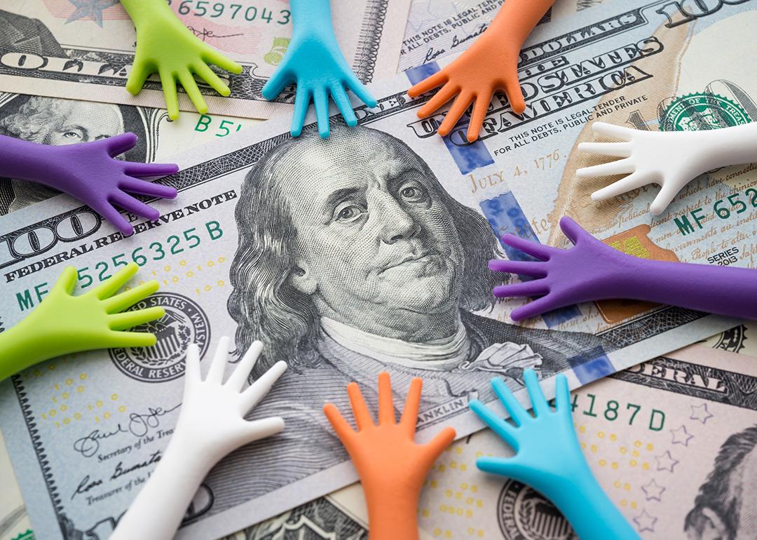 Conceptual image of borrowing money where small figures of hands are on top of US dollar bills.