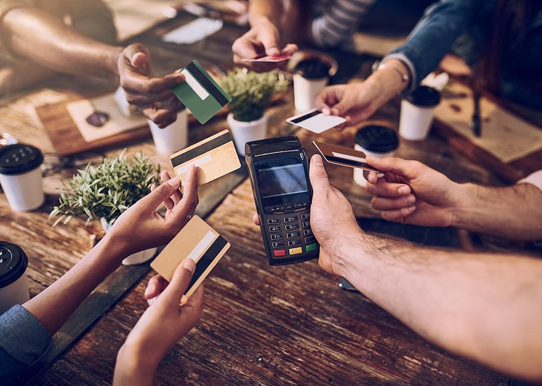 Hands of a group of friends each offering to pay the bill with their credit card.