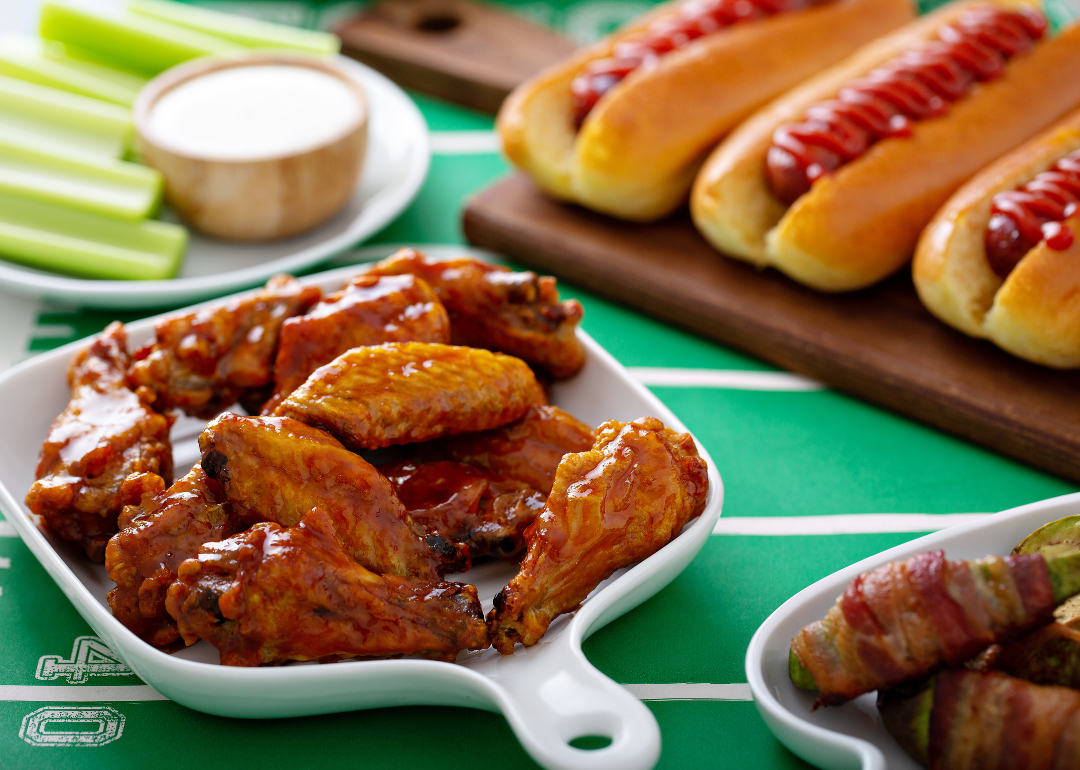 A table with glazed chicken wings, hot dogs, celery sticks and dip