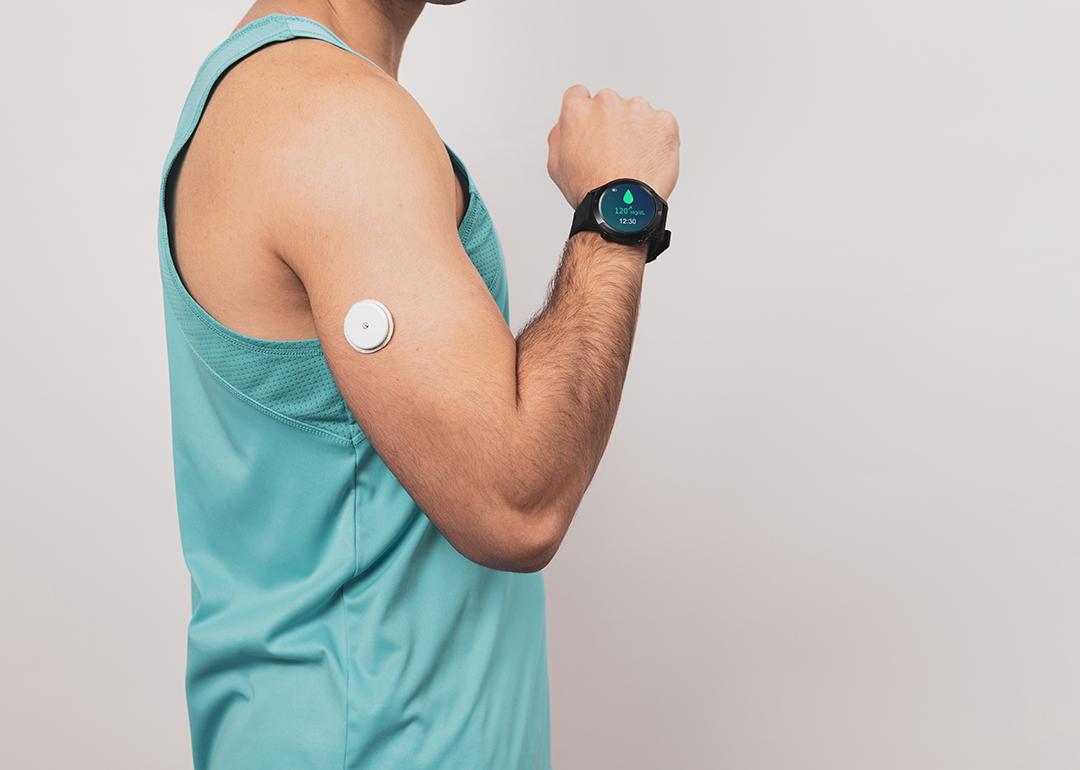 A fit young man monitors blood sugar with a glucose patch and a smartwatch.