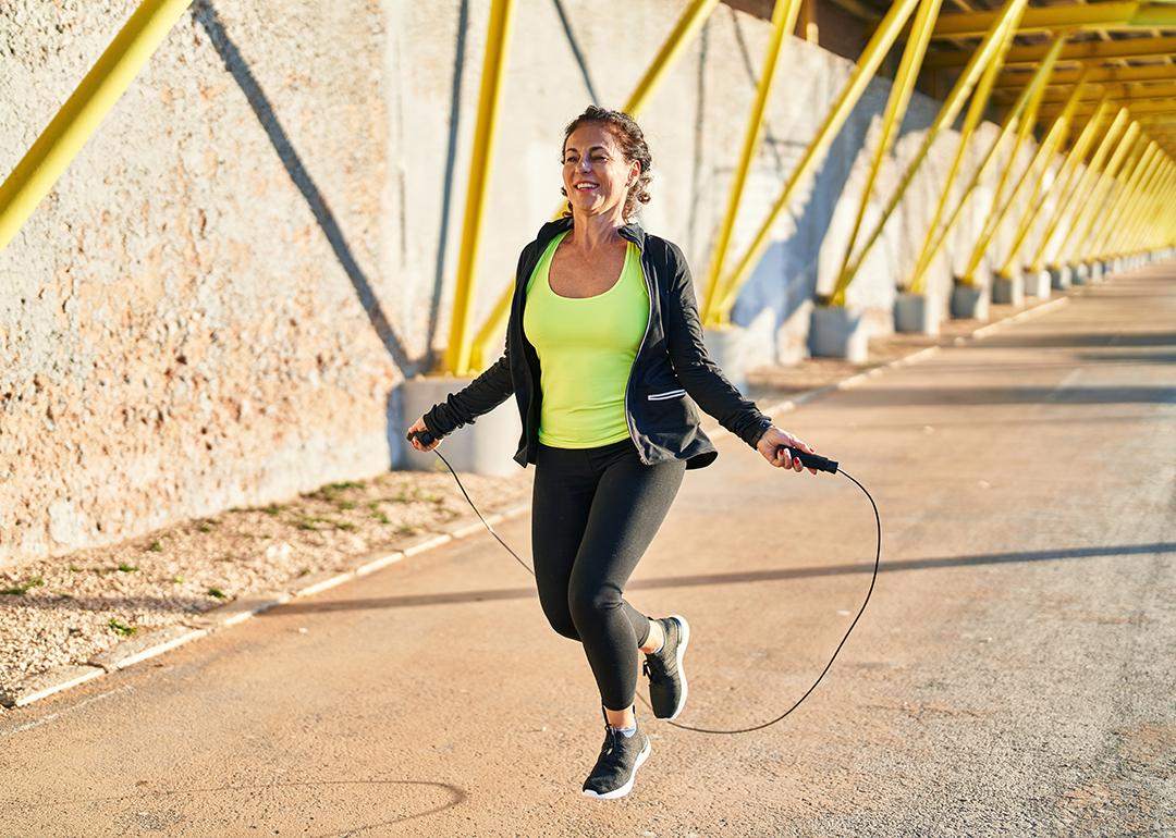 Middle-aged hispanic woman working out outdoors using a jumping rope.