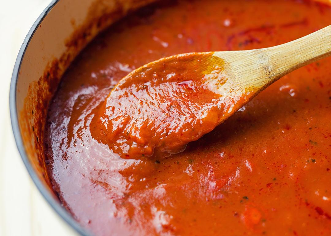 A thick, rich and slow-cooked marinara sauce being stirred in a Dutch oven.