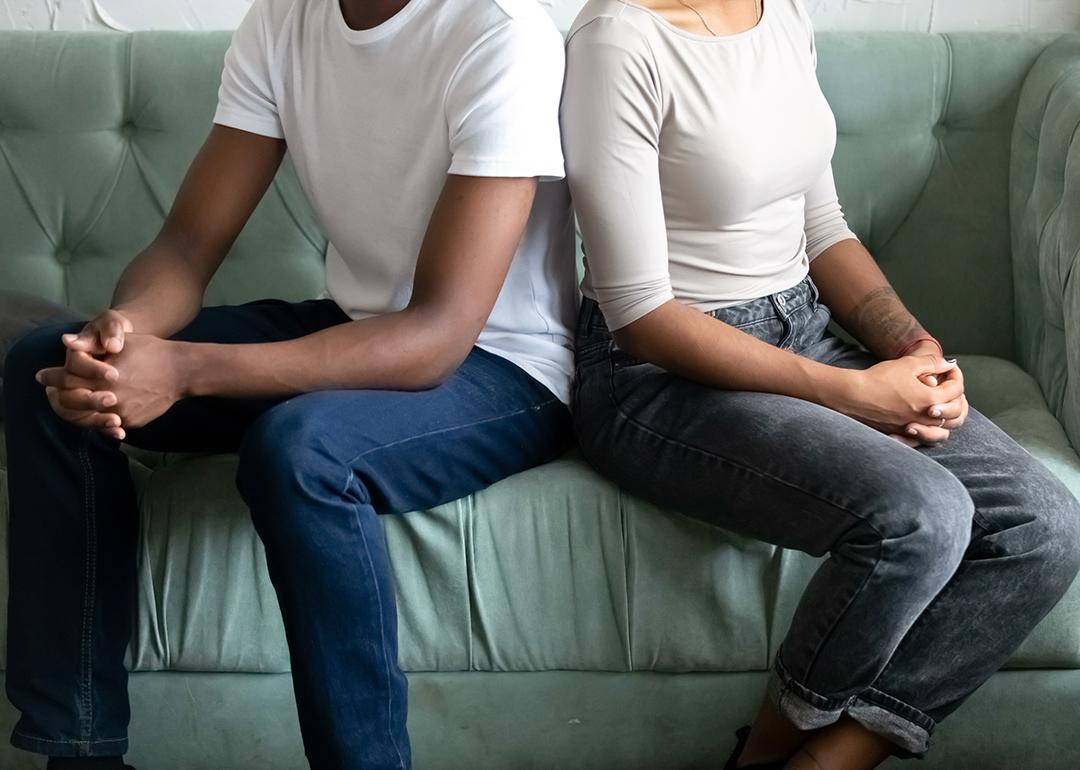 A couple sitting on a couch whose backs are turned on each other.